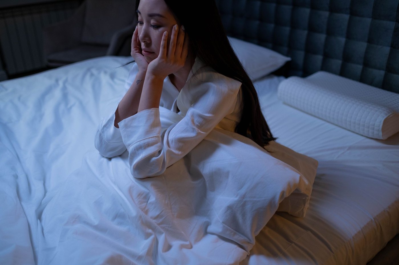 Mujer despierta en la cama con la mano en la mejilla por dolor