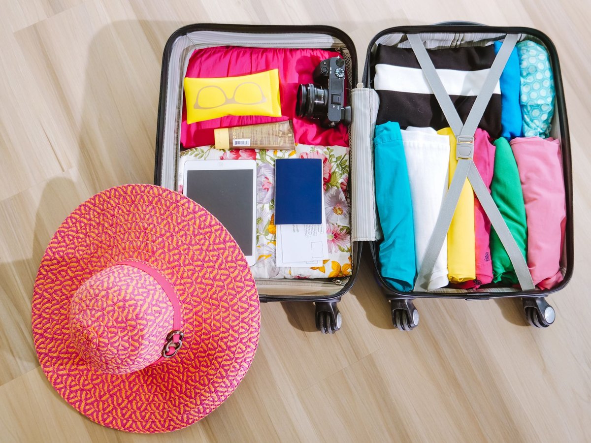 Maleta abierta y preparada con ropa de verano, sombrero y pasaporte