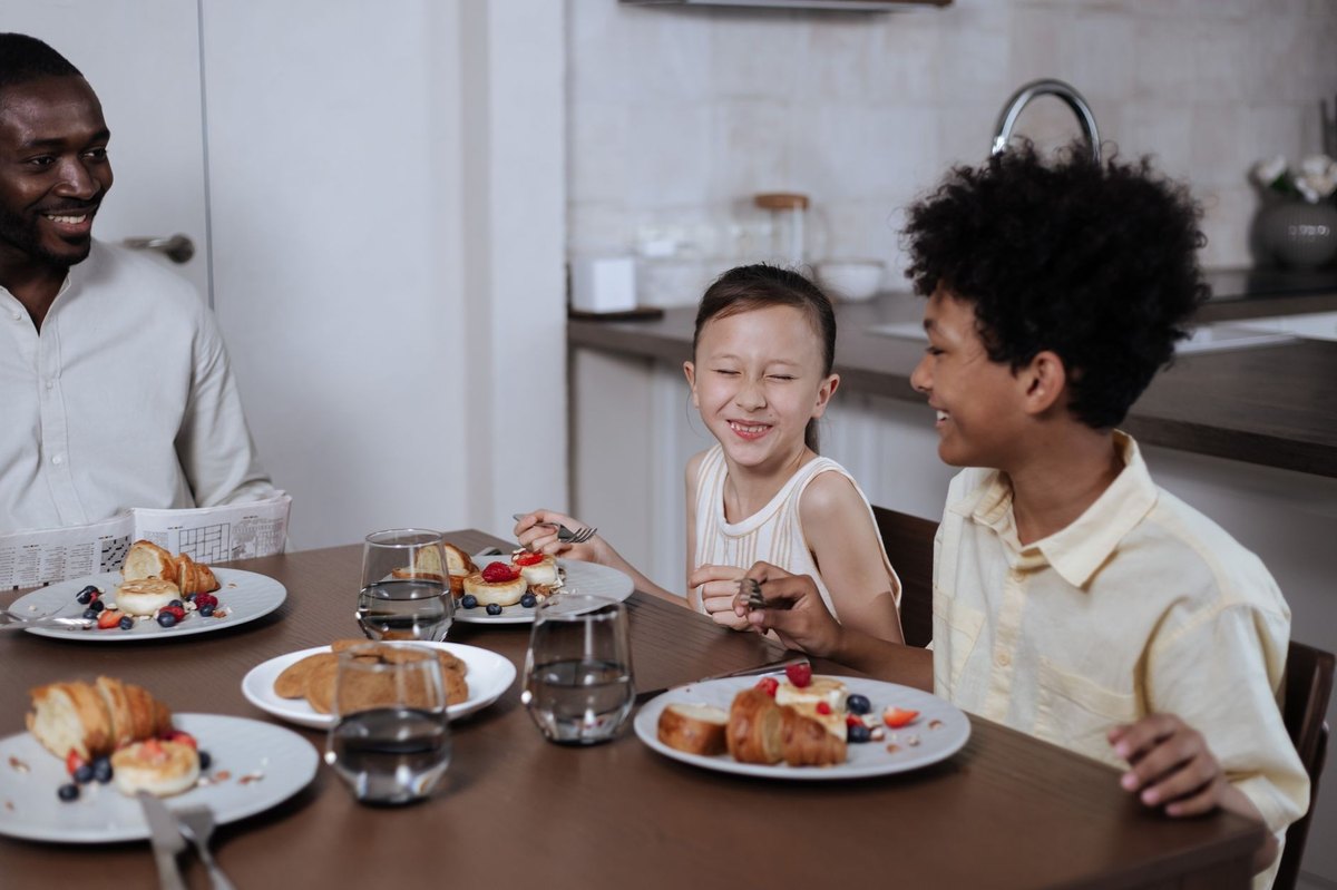 Dos hermanos desayunando juntos en la mesa de la cocina con su padre