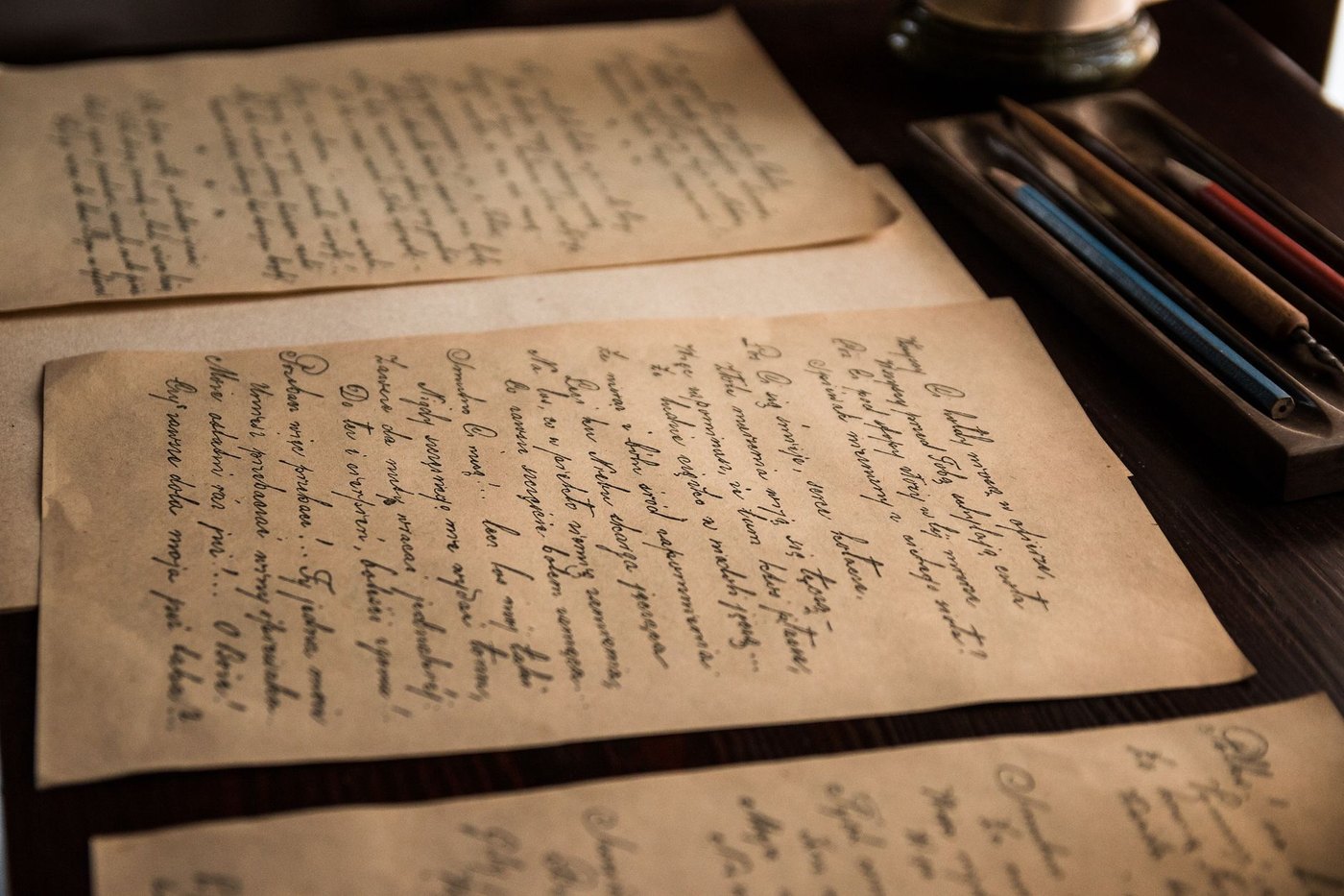 Cartas manuscritas antiguas sobre un escritorio de madera junto a plumas y lápices