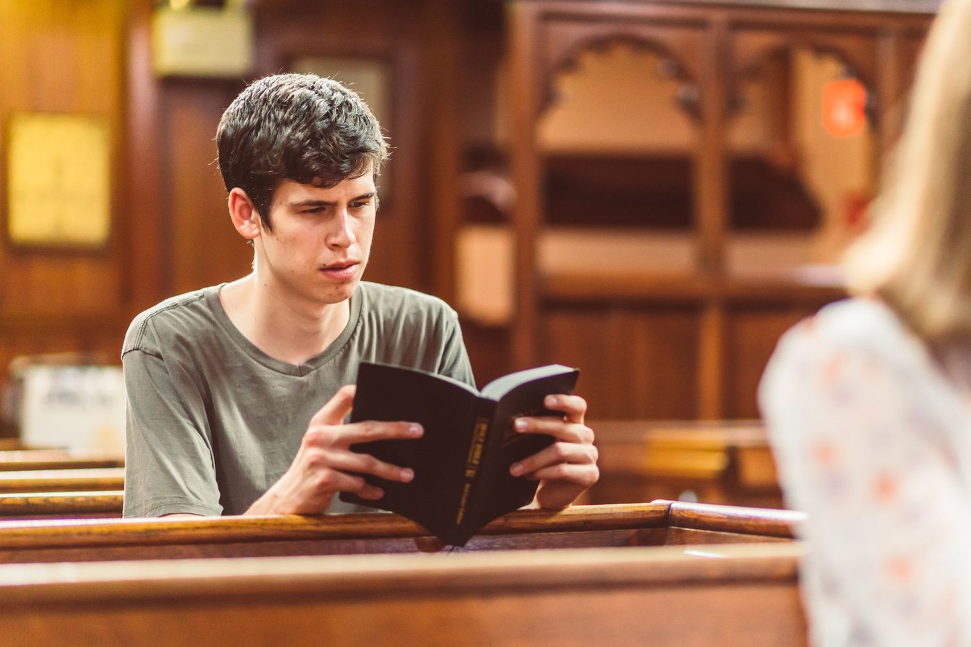 Un joven lee la Biblia sentado en un banco de iglesia