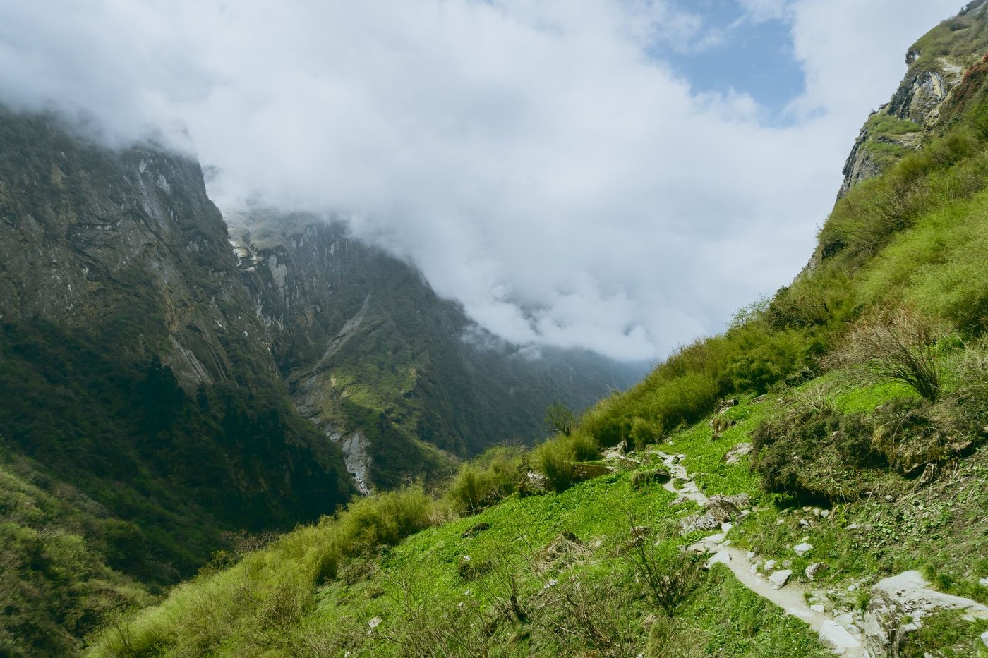 Sendero de piedra ascendiendo por la ladera de un valle de montaña entre nubes