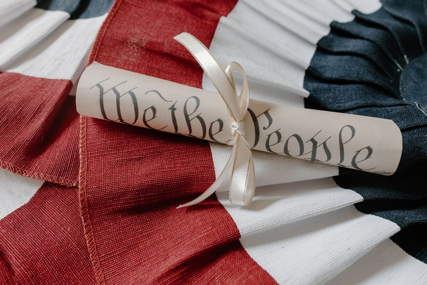 Pergamino enrollado con el encabezamiento «We the People» sobre una tela con los colores de la bandera estadounidense