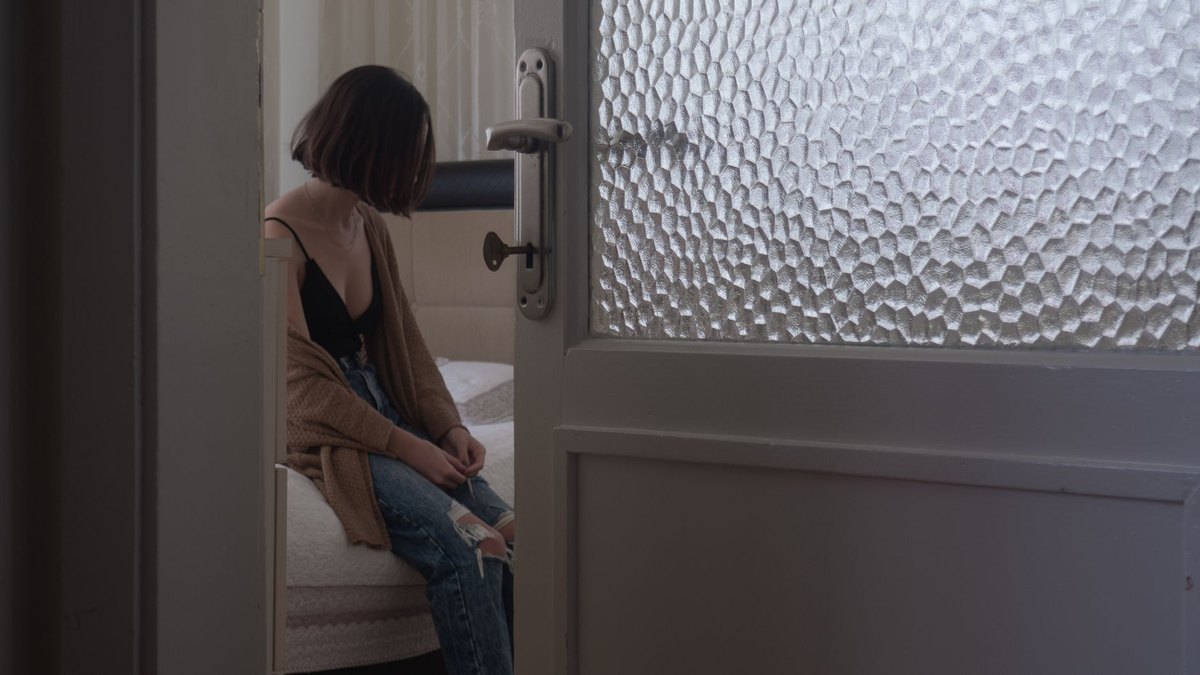 Adolescente sentada a solas en su habitación, vista desde la puerta entreabierta