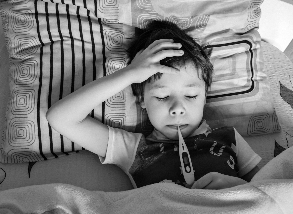 Niño enfermo en la cama con un termómetro
